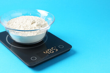 Electronic kitchen scale with flour on light blue background, closeup. Space for text