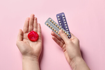 Woman holding blisters of contraceptive pills and condom on pink background, closeup