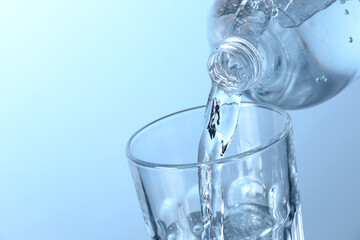 Pouring soda water from bottle into glass on light background, closeup. Space for text