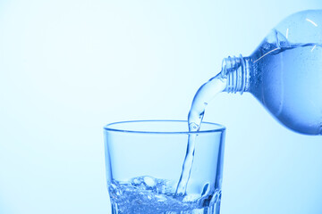 Pouring soda water from bottle into glass on light blue background, closeup. Space for text