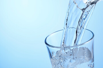 Pouring refreshing soda water into glass on light blue background, closeup. Space for text