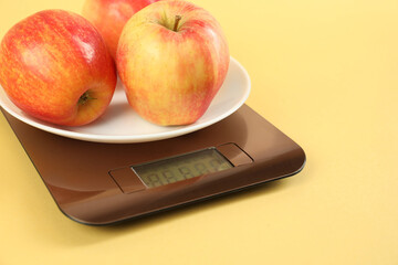 Electronic kitchen scale with apples on yellow background, closeup