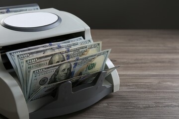 Money counter machine with dollar banknotes on wooden table, closeup. Space for text