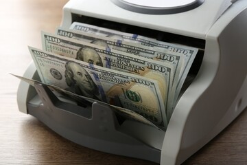 Money counter machine with dollar banknotes on wooden table, closeup