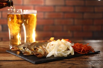 Pouring beer into glass and different dried fish snacks on wooden table. Space for text