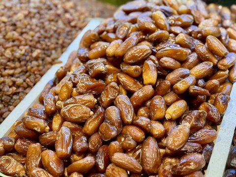 Ripe dark dates are laid out on a tray for sale in a supermarket with an emphasis on the rich quality and color of dried fruits. Close-up