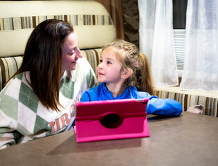 Mom and daughter enjoying time together while using a tablet in their camper van, creating lasting...
