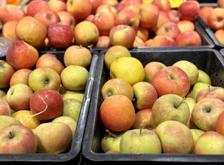 A mound of large red yellow coloured apples in boxes is displayed in the window of the supermarket's vegetable stand, demonstrating organic, vegetarian and healthy food. Close-up