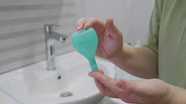 Close-up silicone menstrual cup in woman hand at bathroom. Alternative ecological feminine hygiene product during menstruation waste-free concept