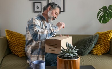 Fototapeta premium Man opening package on cozy sofa with plant