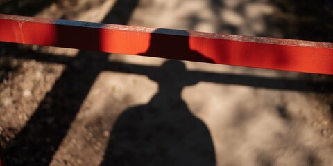 A shadowed figure is seen behind a red barrier on a path, creating an air of mystery and the suggestion of obstacles or challenges that may lie ahead in life.