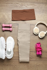 Flat lay composition with women's sportswear and athletic equipment on wooden background