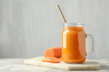 Fresh carrot juice in mason jar and vegetable on gray textured table, space for text