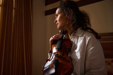 Woman peacefully holding a violin near a window with soft lighting