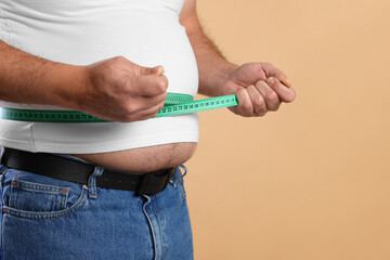 Overweight man measuring his belly with tape on beige background, closeup. Space for text
