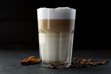Tasty latte macchiato in glass, coffee beans and cinnamon on black table, closeup