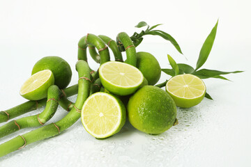 Fresh limes and bamboo stems on wet surface against white background