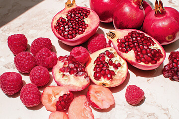 Still life featuring vibrant pomegranates and raspberries on a marble surface under bright lighting