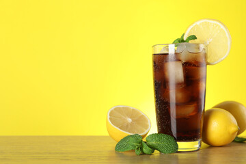 Refreshing iced cola with mint and lemons on wooden table. Space for text