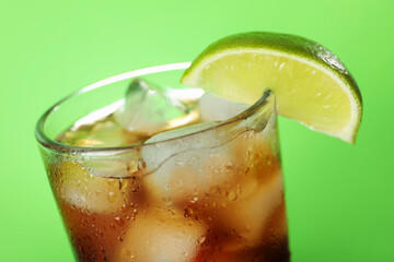 Refreshing iced cola with lime slice on green background, closeup