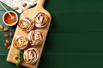 Tasty apple roses with powdered sugar served on green wooden table, flat lay. Space for text