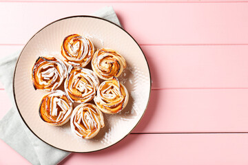 Tasty apple roses with powdered sugar on pink wooden table, top view. Space for text