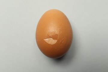 One egg with cracked shell on light grey background, closeup
