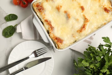 Delicious spinach lasagna in baking dish served on white table, flat lay