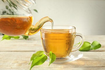 Pouring freshly brewed tea from teapot into glass cup on wooden table, closeup