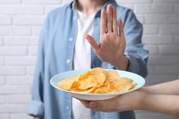 Woman refusing chips near white brick wall, selective focus. Food allergy concept