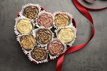 Flower shaped chocolate bonbons in box and red ribbon on grey table, top view