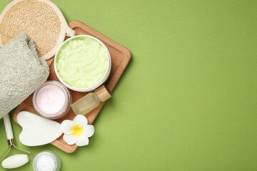 Different body care products and plumeria flower on green background, flat lay. Space for text