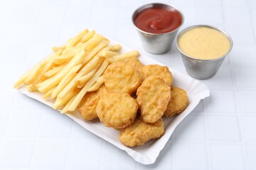 Tasty chicken nuggets and french fries with sauce on white tiled table, closeup
