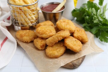 Tasty chicken nuggets, potato fries and ketchup on white tiled table, closeup