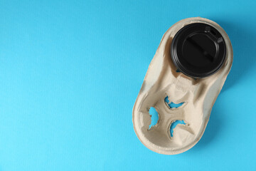 Paper coffee cup in cardboard holder on light blue background, top view. Space for text