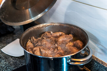 Chef preparing chicken broth with heads, necks, and legs in stainless steel pot, to make collagen gelatins