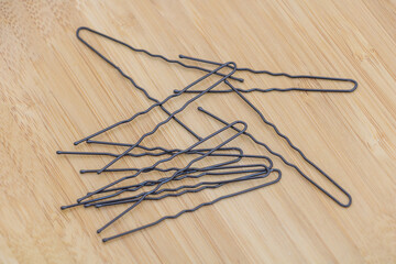A set of hair pins, thin black metal clips on a light wooden table, top view