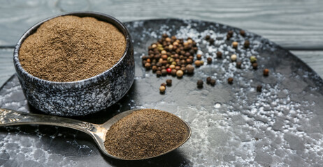 Board with black pepper powder and peppercorns on dark wooden background