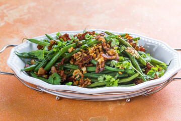 Delicious green beans salad with bacon, orange, peanuts, garlic and spices on a plate. Healthy warm salad idea.