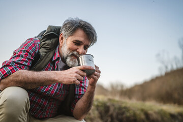 man hiker backpacker kneel by a creek and filling a mug with water