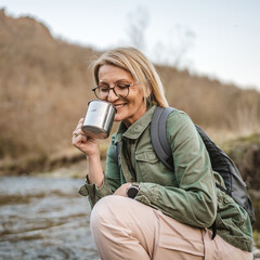 woman hiker backpacker kneel by a creek and filling a mug with water