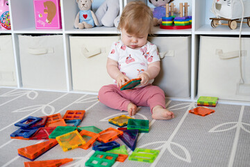 Cute Caucasian baby girl playing with magna tiles. Magnetic tiles toys. Baby playing with toys. Early childhood. 