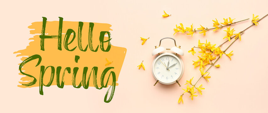 Blooming tree branches with yellow flowers and alarm clock on beige background