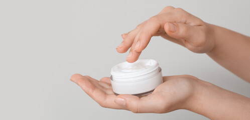 Female hands with jar of cosmetic cream on grey background