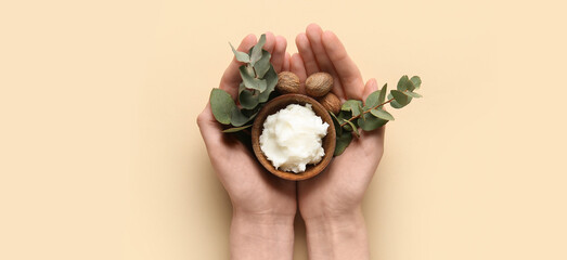 Female hands holding green twig, bowl with shea butter and nuts on beige background
