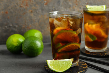 Glasses of cold Cuba Libre cocktail and limes on grey table