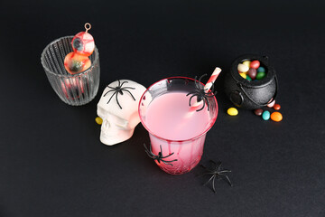 Glass of tasty Margarita cocktail with skull and treats for Halloween on black background