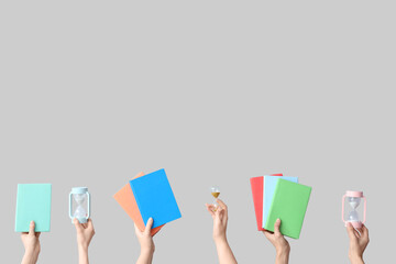 Female hands holding hourglasses and books on grey background