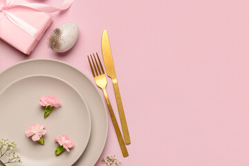 Cute Easter table setting with gifts, flowers and eggs on pink background