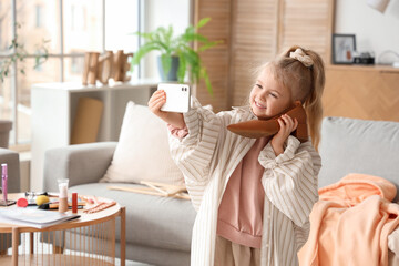 Cute little girl in adult clothes with heel taking selfie at home